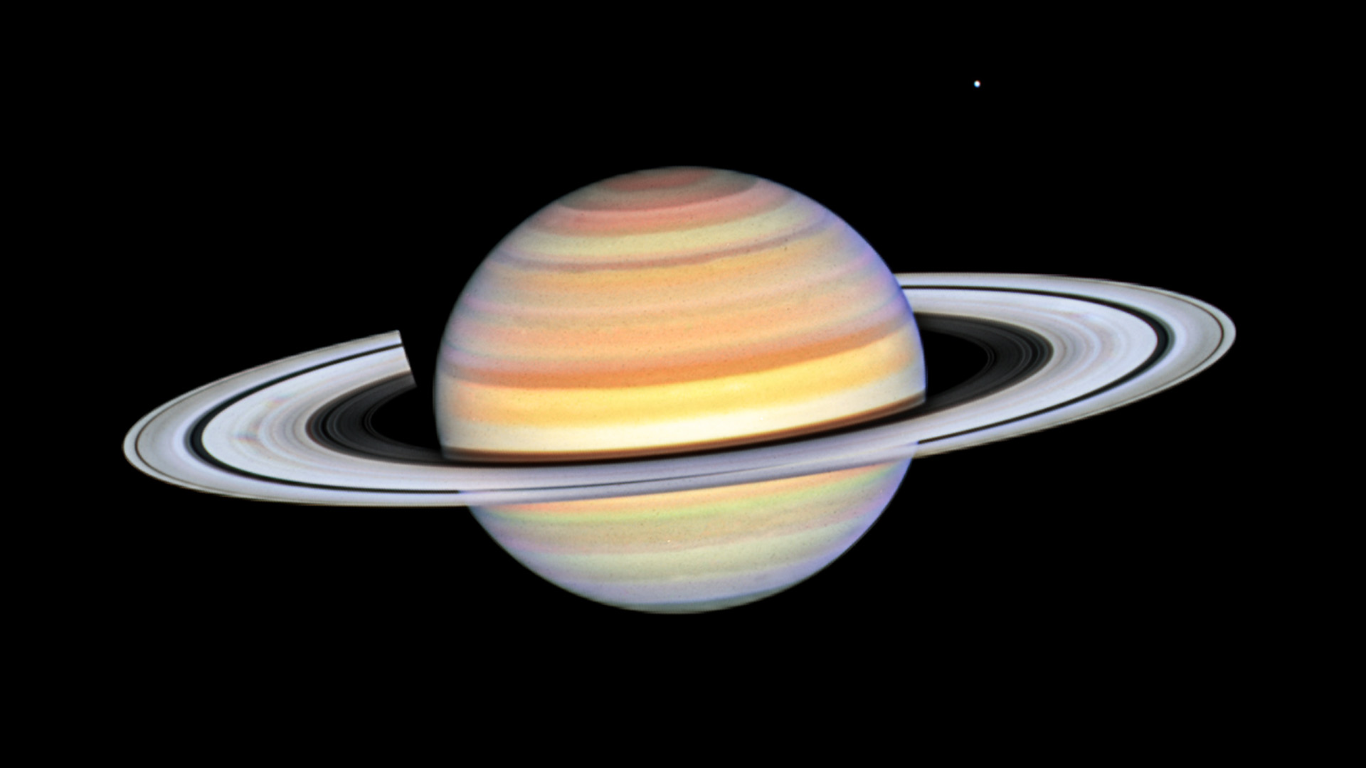 Saturn with its prominent gray and black rings against the black expanse of space.
