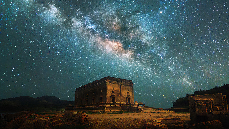 Ruins under a star-filled sky, centered is the Milky Way.